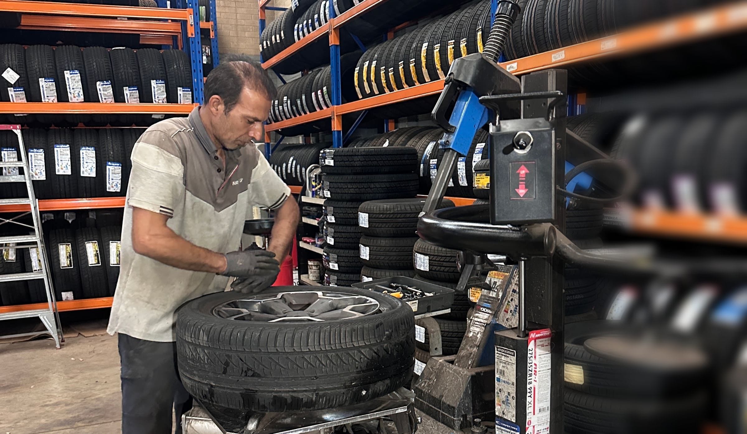 A man working at the tyre changer in the SA Tyre & Auto workshop, with racks of tyres behind him